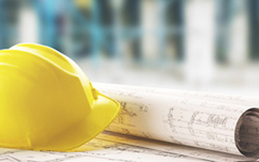 Ein Bauhelm liegt auf einem Tisch mit Planzeichnungen. Foto: ALDECAstudio/Fotolia