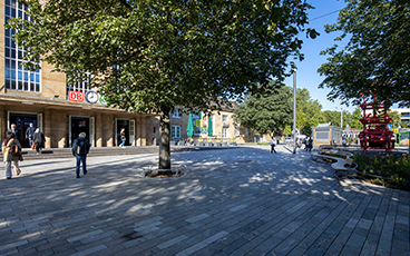 Der neue Bahnhofsplatz mit Bäumen, einer Sitzbank und Blick auf den Haupteingang des Cannstatter Bahnhofs.