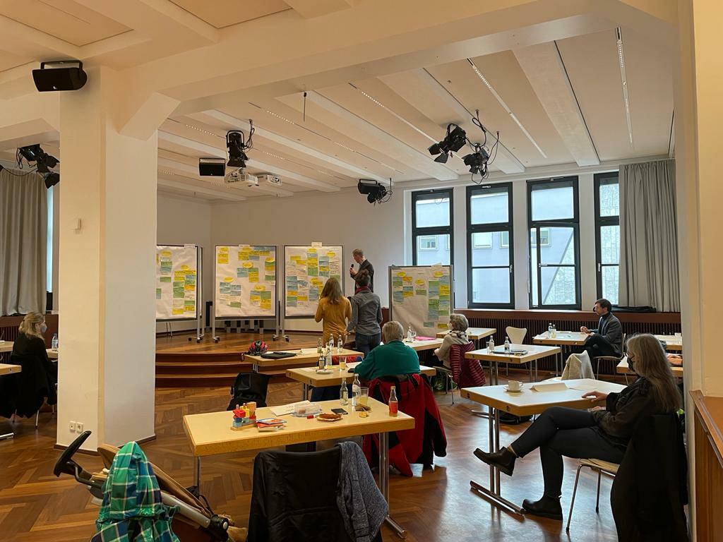 In einem Saal sitzen die Mitglieder der Bypad-Gruppe und beraten zum Konzept. Im Hintergrund sind STellwände mit Ideen und Anmerkungen zu erkennen.